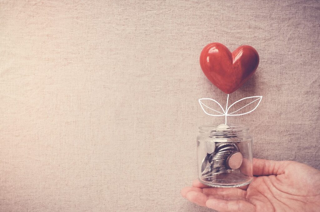 Hand holding a jar of heart tree growing on money coins,charity, social responsible business and donation, fundrasing, relief plan concept