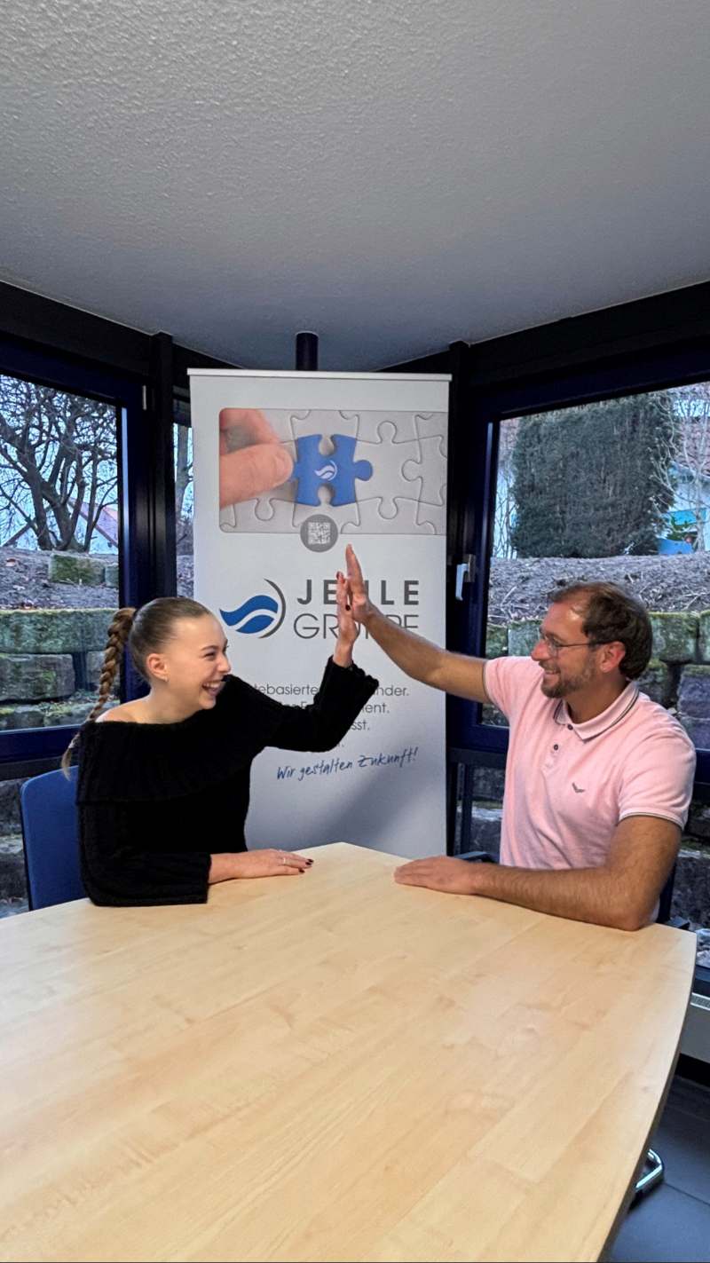 Eine junge Frau in Schwarz und ein Mann in Rosa lächeln und geben sich ein High Five